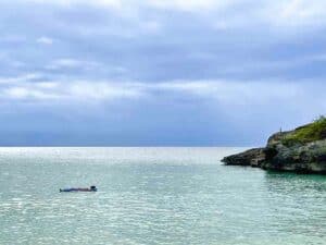 A person is floating in the water near a serene beach cliff in Anguilla.