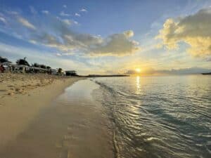 The sun is setting over a beach in Anguilla with chairs and umbrellas.