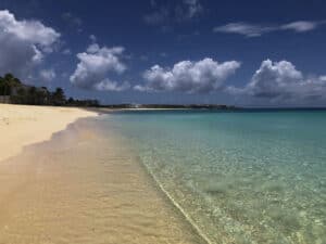 A sandy beach with clear water and white clouds in Anguilla.
